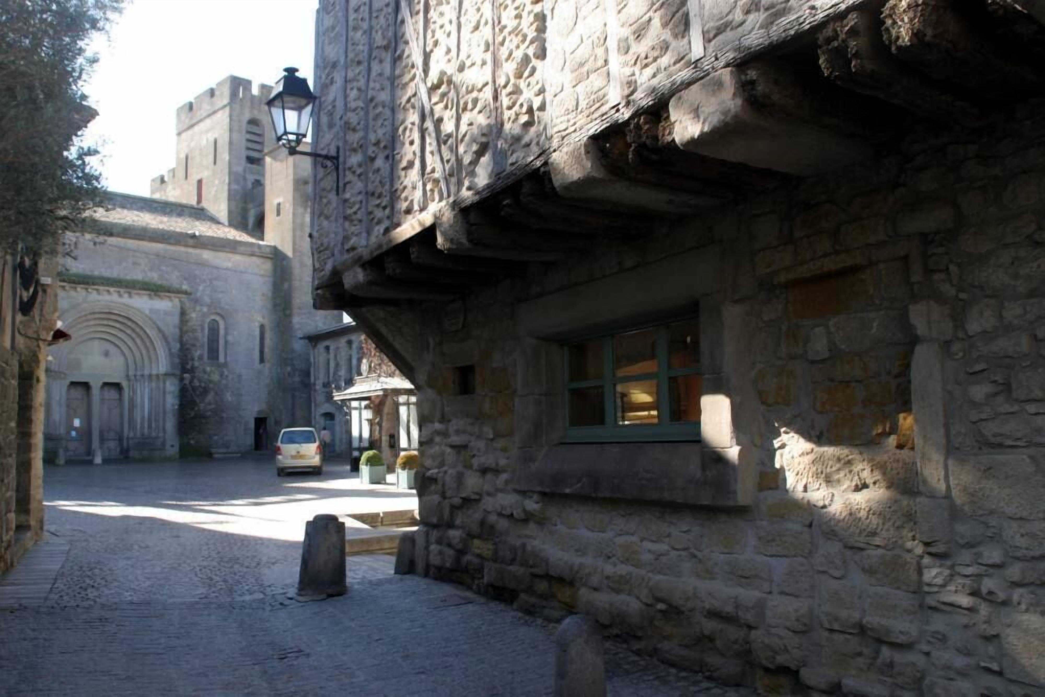 A narrow cobblestone street with a stone building featuring a window with green shutters.
