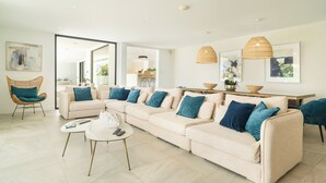 Een moderne woonkamer met een beige hoekbank, een ronde salontafel en een rieten fauteuil.
