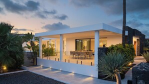 Een modern huis met een terras, zitgedeelte buiten en een goed verlichte ingang.