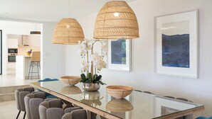 Een moderne eethoek met een glazen tafel, gestoffeerde grijze stoelen en geweven hanglampen.