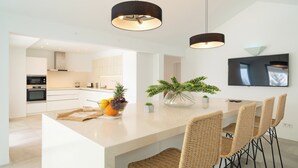 Een moderne keuken met witte kastjes, een centraal eiland met rieten stoelen en een flatscreen televisie aan de muur.
