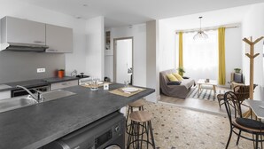 A modern kitchen with a central island, built-in appliances, and a dining area with a table and chairs. - MOSAIK, Charmant appartement Nantais (Nantes)