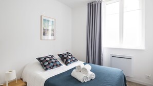 A neatly made bed with a blue bedspread, two pillows with a circular pattern, and rolled towels on the bed. - MOSAIK, Charmant appartement Nantais (Nantes)