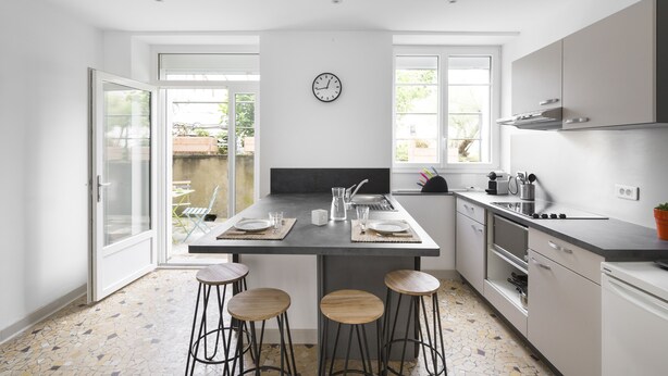 A modern kitchen with a central island, bar stools, and a view to the outside. - MOSAIK, Charmant appartement Nantais (Nantes)