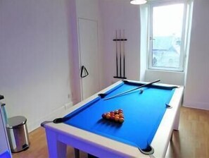 A pool table with balls, a trash bin, and a window with blinds.