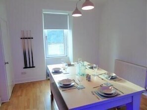 A dining area with a table set for four, a window with blinds, and a radiator on the wall.