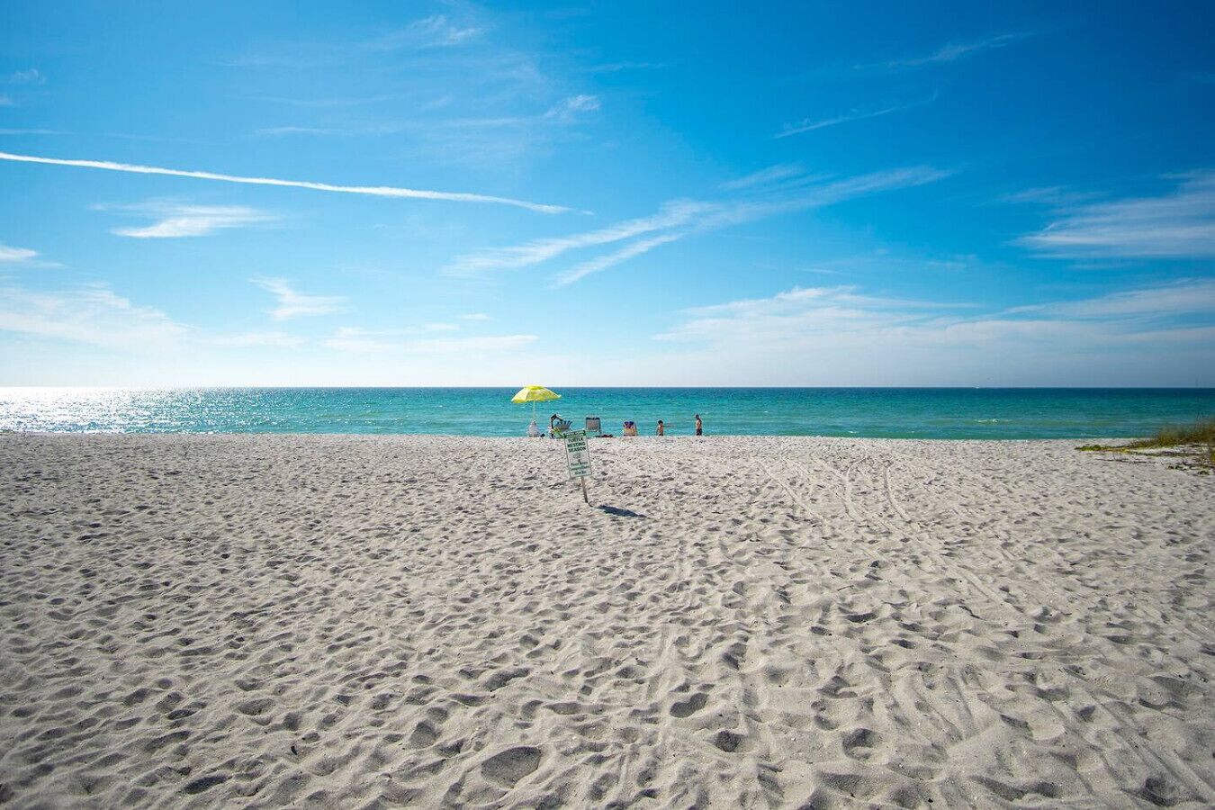 Uma praia arenosa com pegadas que levam a um guarda-sol amarelo.