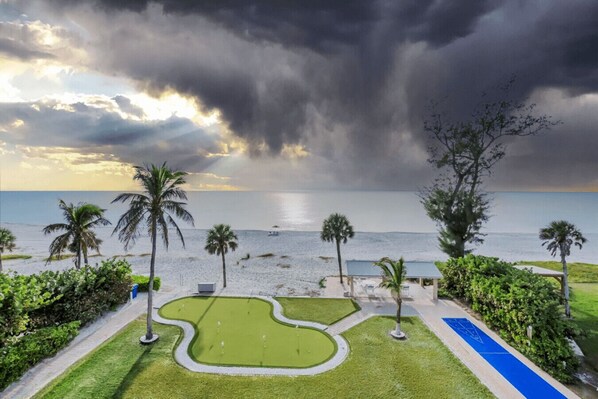 A beach view with palm trees, a grassy area, and a small building.