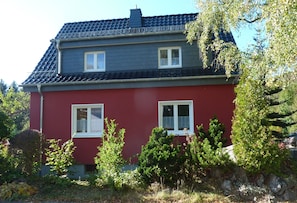 Ein zweistöckiges Haus mit roter Fassade und einem dunkelgrauen Dach.