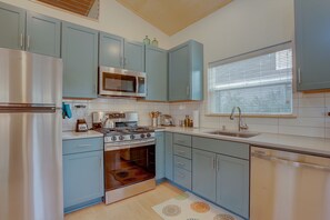 A kitchen with light blue cabinets, stainless steel appliances, and a window with blinds.