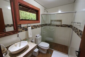 Un baño con cabina de ducha de vidrio, lavabo con encimera de mármol, inodoro y ventana con vistas a zonas verdes.