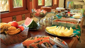 A buffet table with various fruits, a watermelon, and a glass bowl.