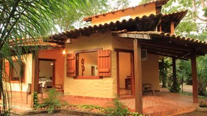 A small, rustic building with a tiled roof and wooden shutters, surrounded by greenery.