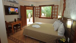 A hotel room with a bed, a desk, a TV, and a window with a view of palm trees.