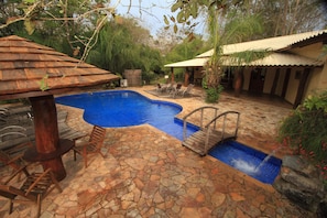 Una piscina con baldosas de piedra, sillones de madera y una pérgola de madera.