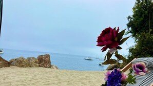 En picnic ved stranden med et træbord, en stribet strandstol og en vase med blomster.