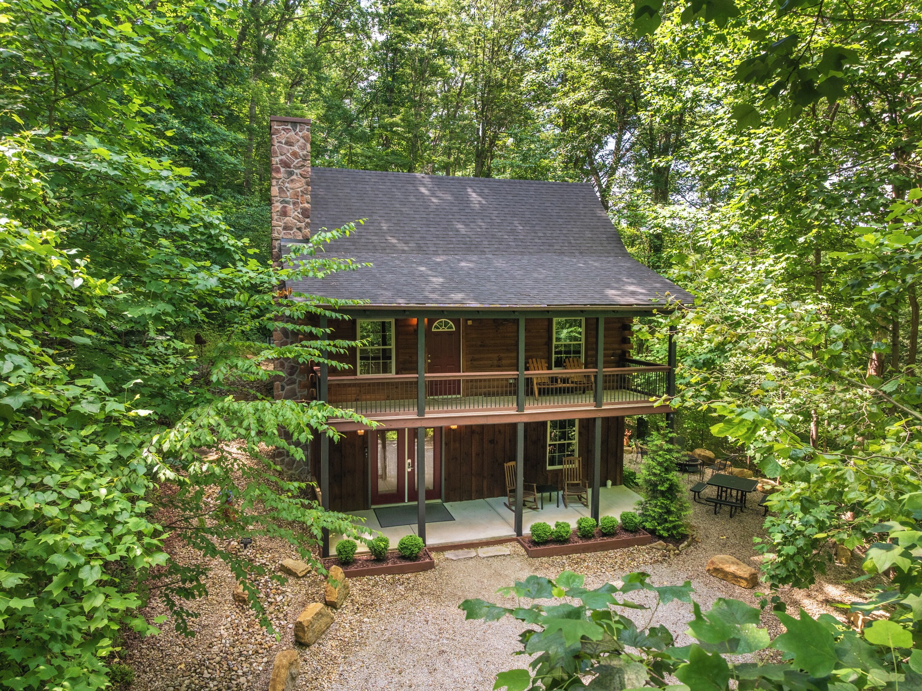 A two-story log cabin with a balcony, surrounded by dense forest.