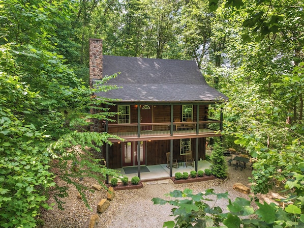A two-story log cabin with a balcony, surrounded by dense forest.