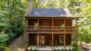 Eine zweistöckige Holzhütte mit Balkon, umgeben von einem Wald.