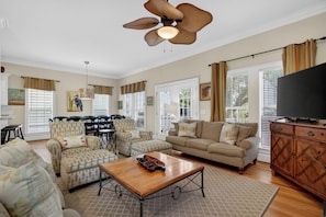 A living room with a sofa, armchairs, a coffee table, a TV, and a ceiling fan.