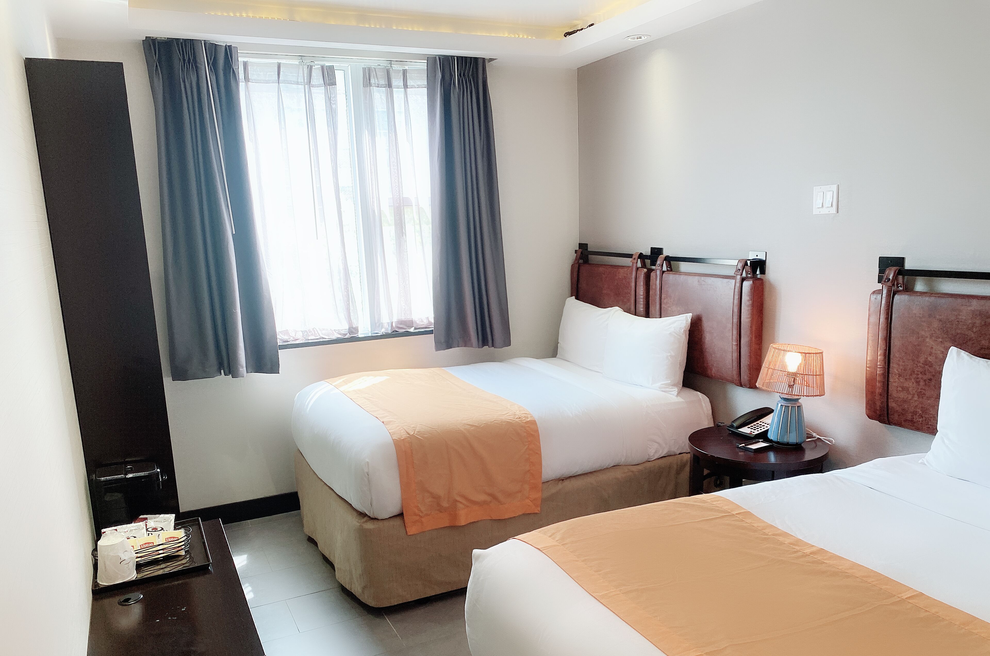 Una habitación de hotel con dos camas, una mesita de noche con lámpara y una ventana con cortinas.