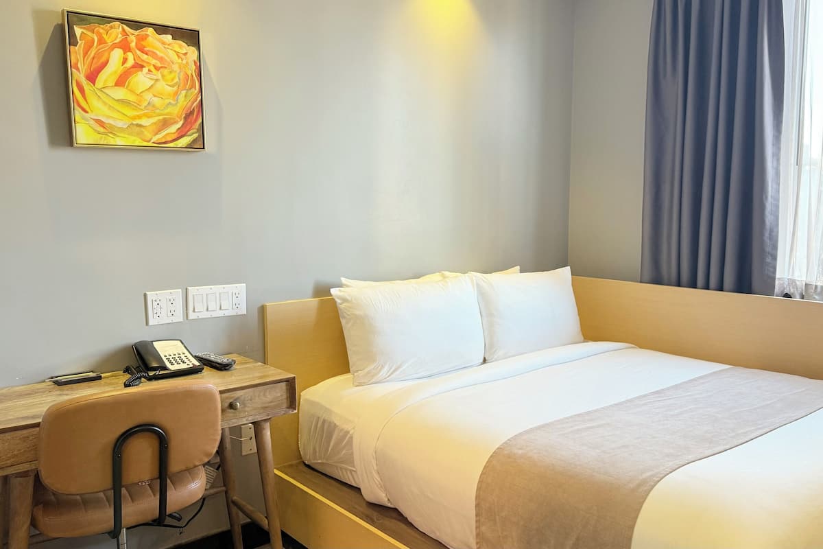 Habitación de hotel con cama, escritorio, teléfono, una silla y un cuadro en la pared.