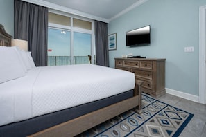 A bedroom with a large bed, a dresser, a flat-screen TV, and a balcony with curtains.