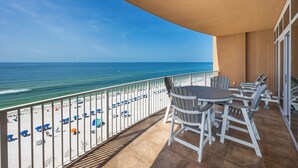 A balcony with a view of the beach and ocean. There are chairs and a table on the balcony.