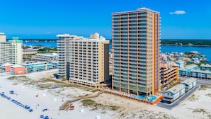 A beachfront hotel with multiple high-rise buildings, a sandy beach with umbrellas, and a clear view of the ocean.