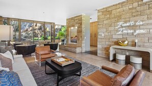Een moderne woonkamer met een stenen openhaard, leren banken en een groot raam met uitzicht op een tuin.
