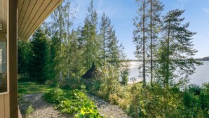 A view from a wooden deck overlooking a lake, surrounded by dense trees and a small cabin. - Kärkiniemi (Tuusniemi)