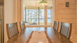 A wooden dining table with a woven placemat, six wooden chairs, and a hanging pendant light. - Kärkiniemi (Tuusniemi)