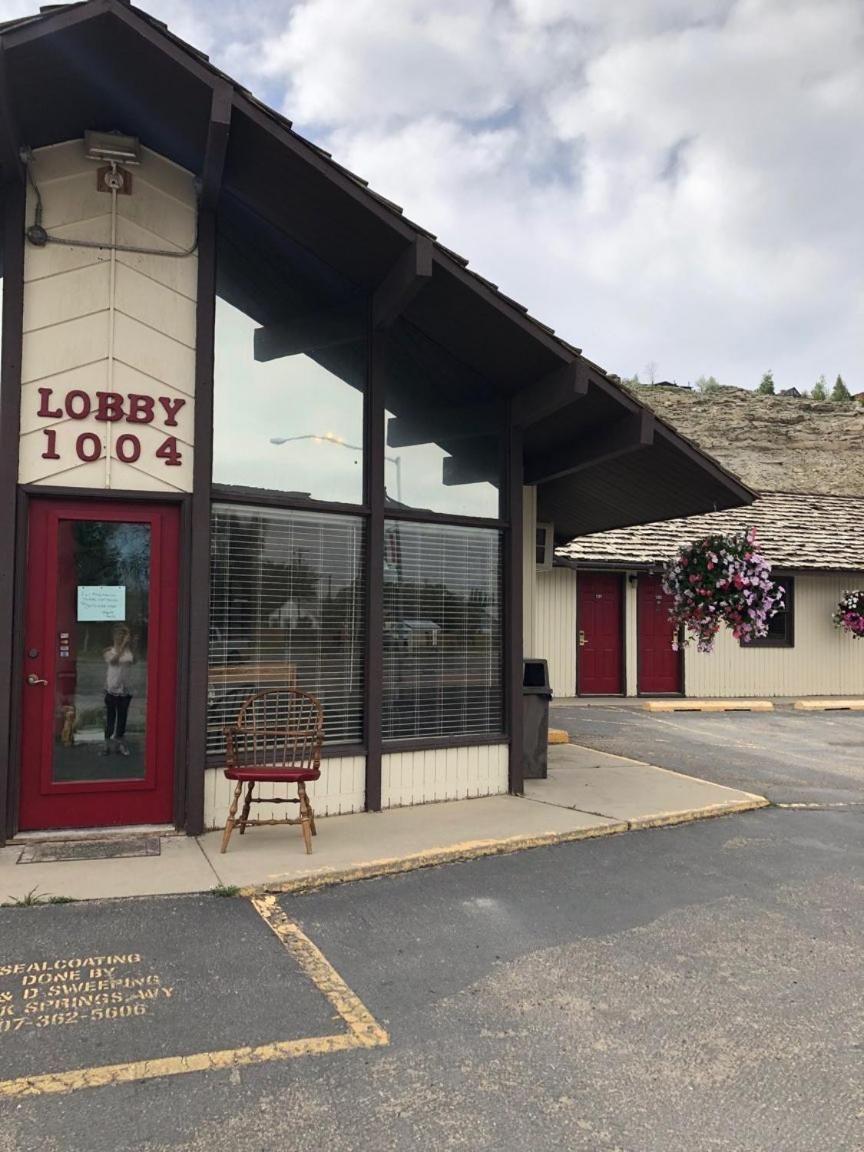 A building with a red door labeled 'Lobby 1004' and a covered area with a chair and hanging flowers.