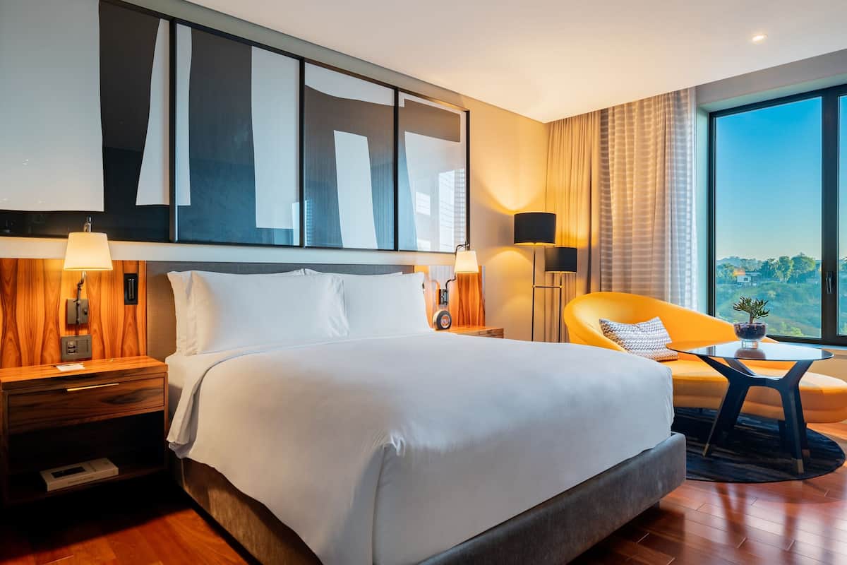 Een moderne hotelkamer met een groot bed, een slaapbank, een tafeltje en uitzicht op de skyline.