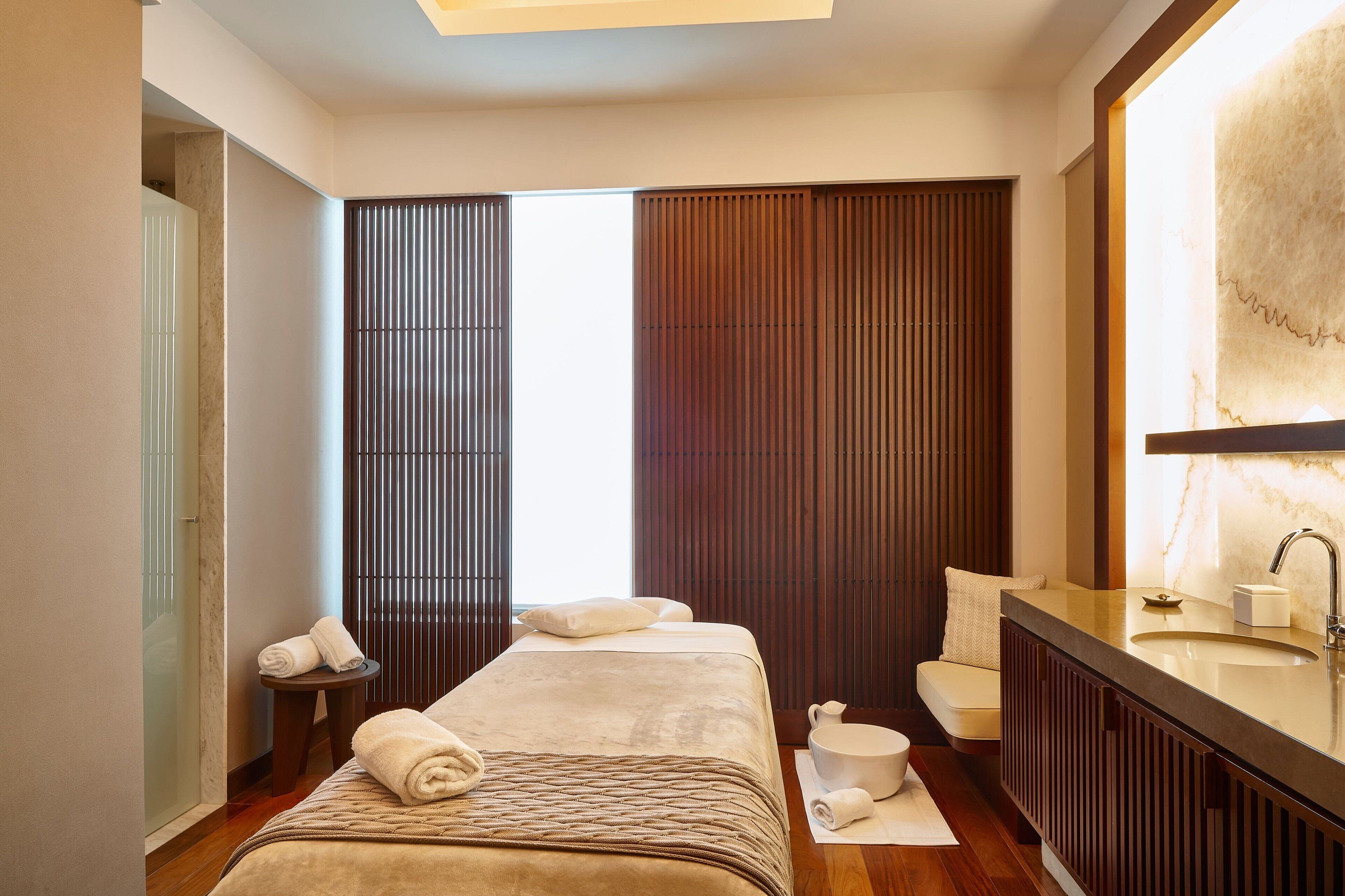A modern hotel room with a large bed, a sitting area, a bathroom with a large mirror, and a view of the city.
