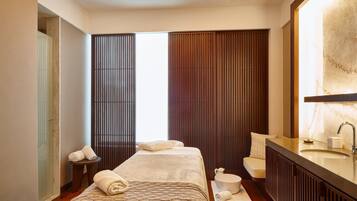 A modern hotel room with a large bed, a sitting area, a bathroom with a large mirror, and a view of the city.