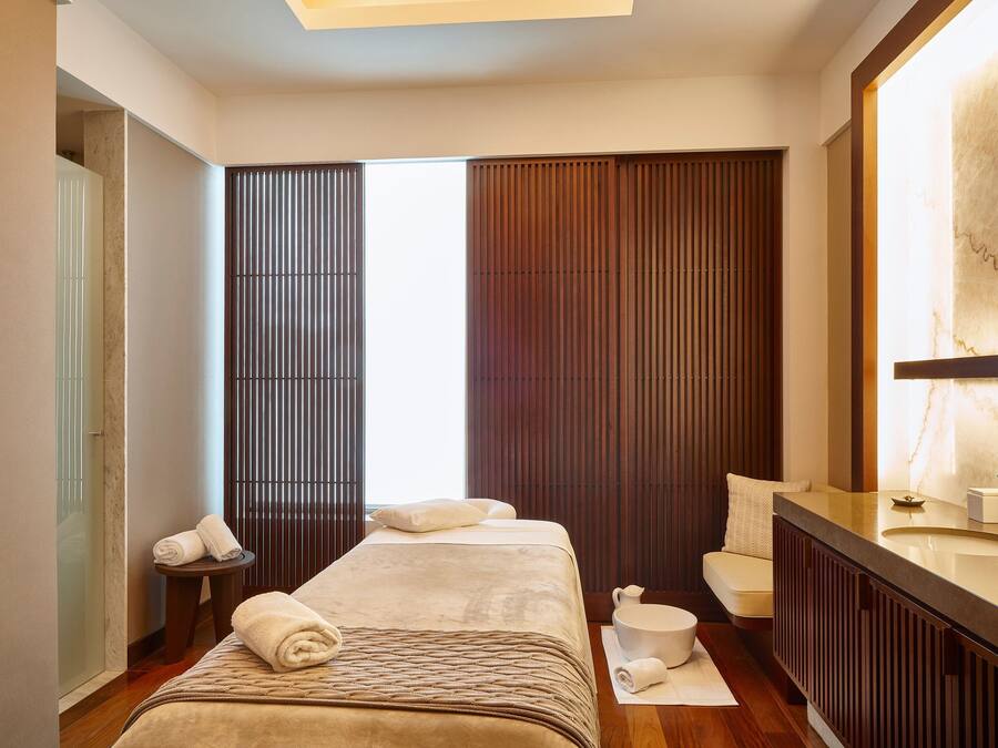A modern hotel room with a large bed, a sitting area, a bathroom with a large mirror, and a view of the city.