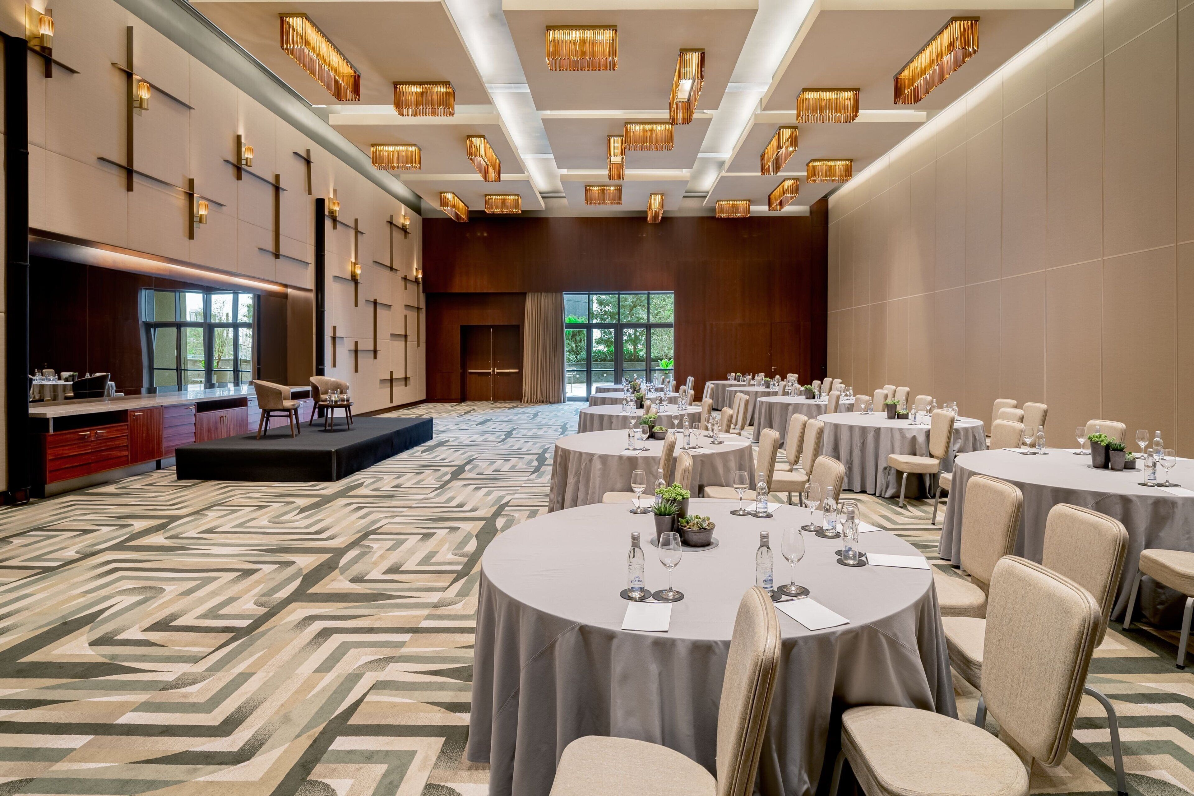 A spacious banquet hall with round tables, chairs, and a stage.