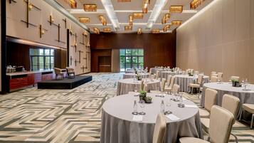 A spacious banquet hall with round tables, chairs, and a stage.