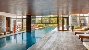 Une piscine intérieure avec des parois en verre transparent, des fauteuils de relaxation en osier et un design de plafond moderne.
