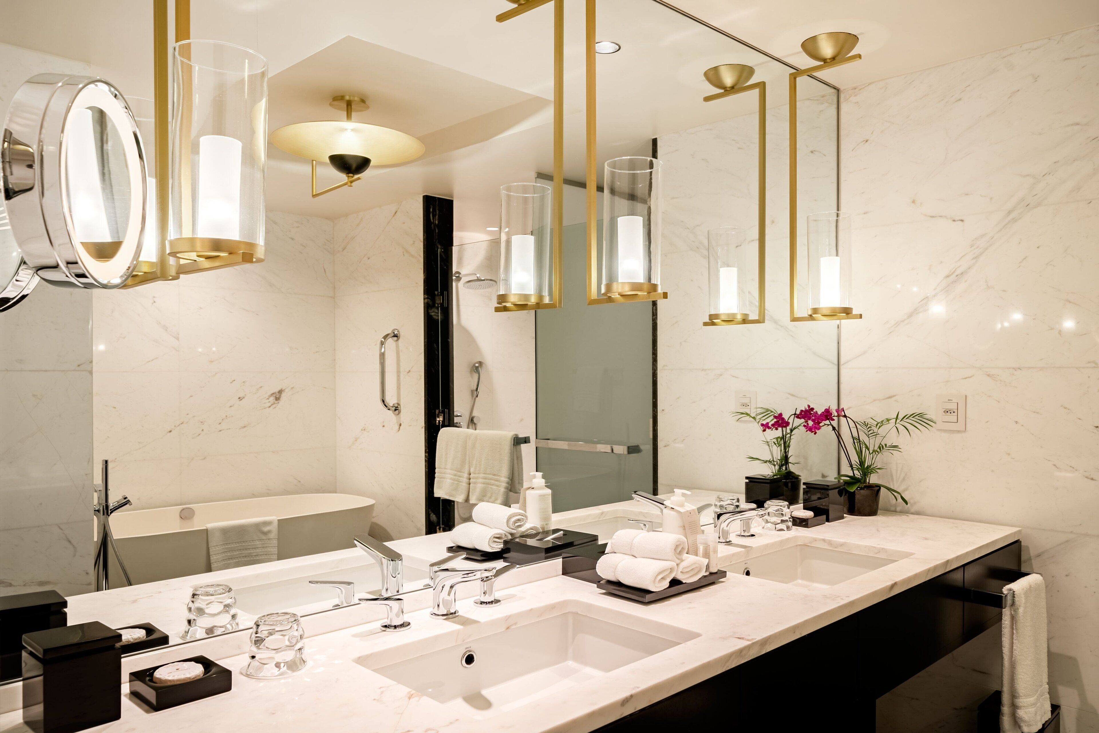A modern bathroom with dual sinks, a large mirror, and gold fixtures.