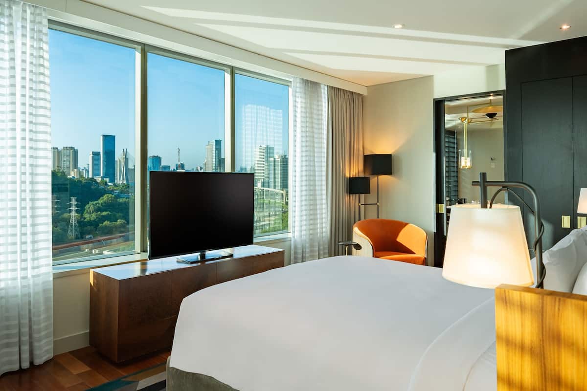 Hotelkamer met een groot bed, televisie, bureau en stoel. Er is een raam met uitzicht op de stad.