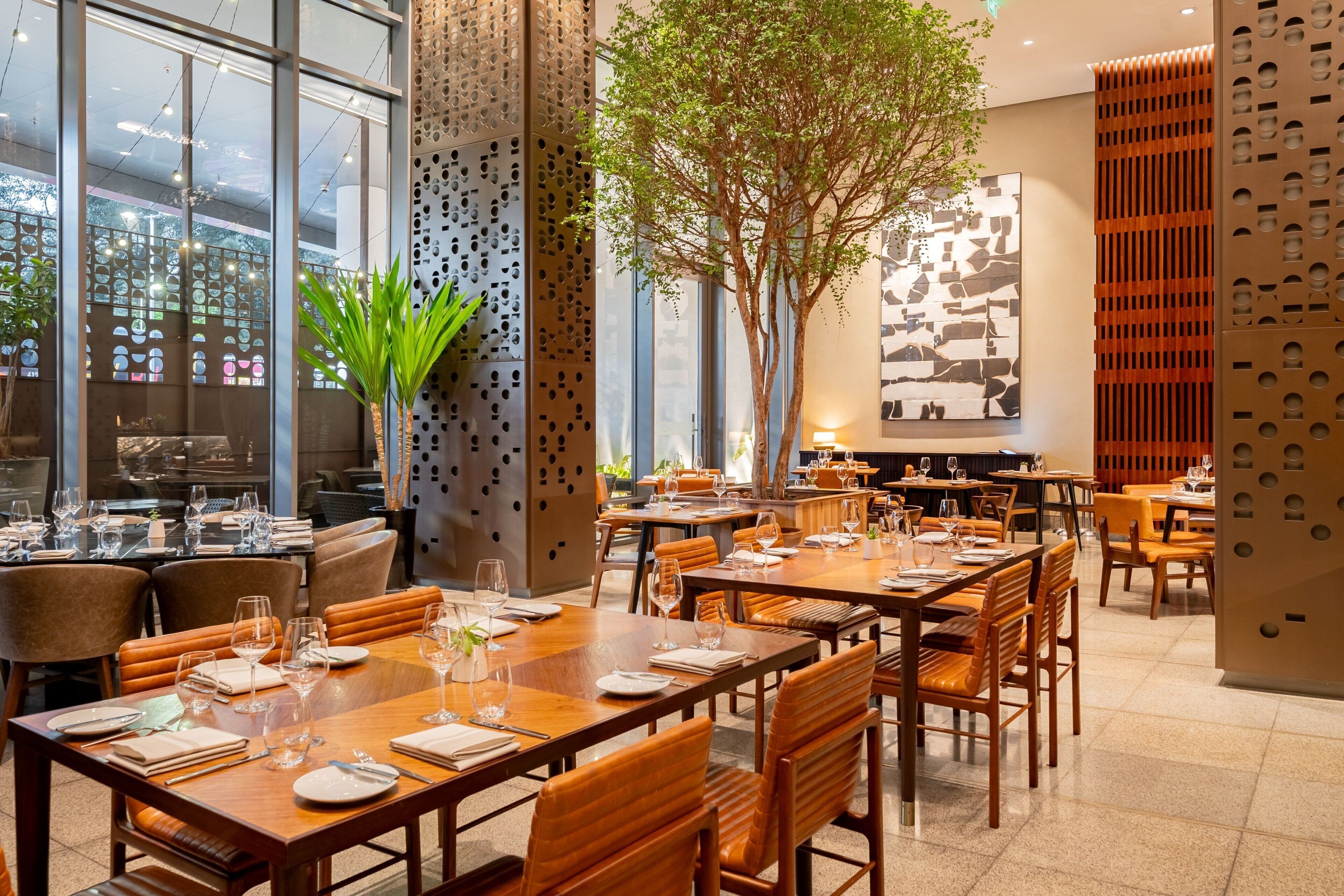Un restaurante con varias mesas, sillas y un gran árbol en el centro.