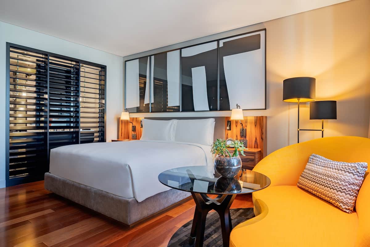 Een moderne hotelkamer met een groot bed, een glazen tafel, een bank en een groot abstract schilderij boven het bed.