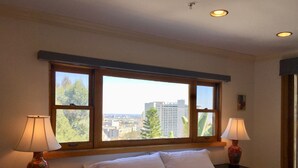A bedroom with a large window, two bedside lamps, a bed with white bedding, and a view of a cityscape. - Classic Hollywood Hills Living with Amazing Views ~1200sf (Los Angeles)