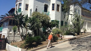 A white building with a red-tiled roof, surrounded by greenery and cacti. - Classic Hollywood Hills Living with Amazing Views ~1200sf (Los Angeles)