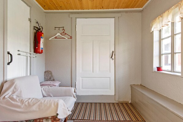 A cozy room with a white door, a fire extinguisher, a radiator, a bench, and a window with curtains. - Savenkaita (Tuusniemi)