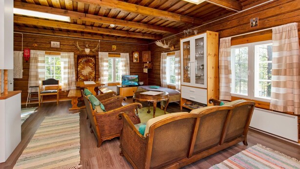 Ein gemütliches Blockhaus-Interieur mit Holzwänden und -decken, einem Essbereich mit Korbmöbeln und einem Fernseher.