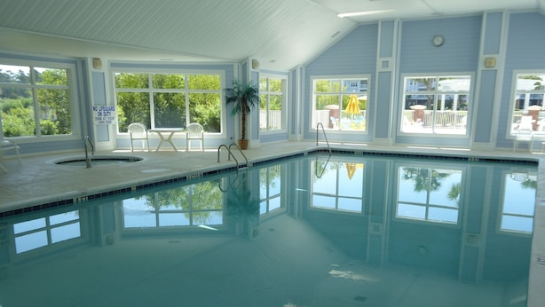 An indoor swimming pool with clear blue water, surrounded by windows offering views of the outdoors.
