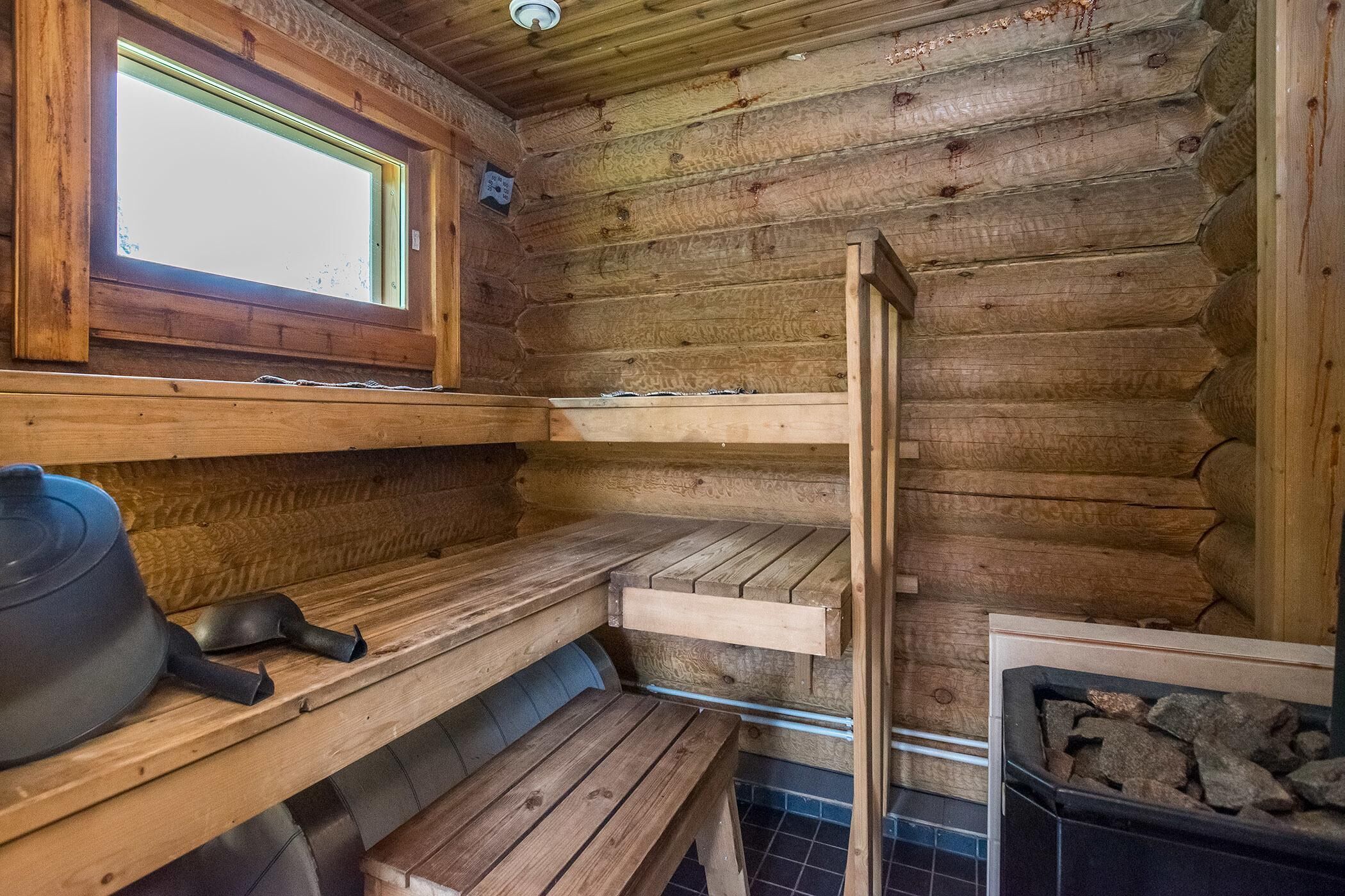 Interior de una cabaña de madera con ventana, banco, mesa y chimenea.